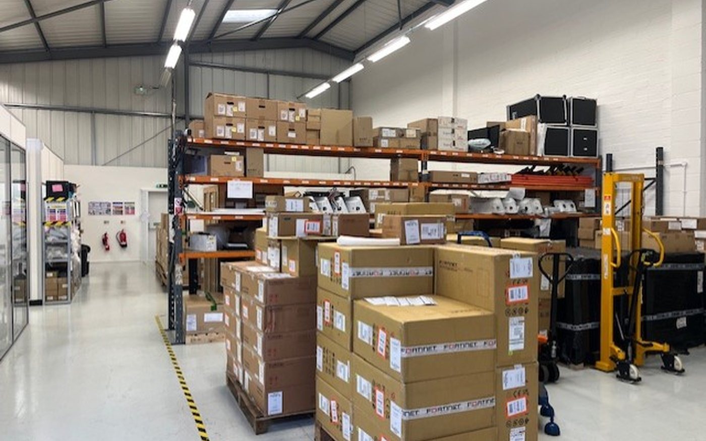 Small warehouse unit with shelving, palletised stock and a pallet truck